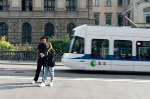Junge Personen am Mobiltelefon auf der Strasse mit Tram im Hintergrund