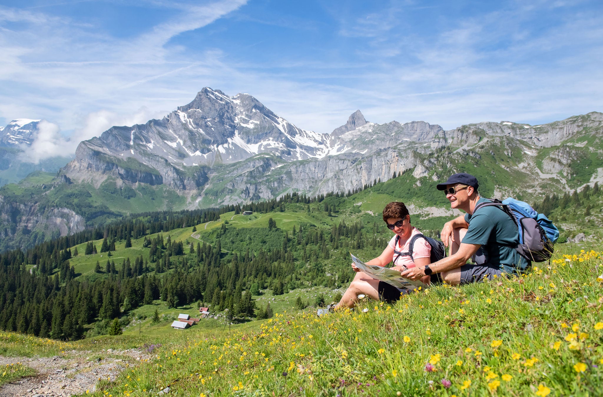 Zwei Personen sitzen auf einer Wiese in Braunwald und halten eine Karte. 