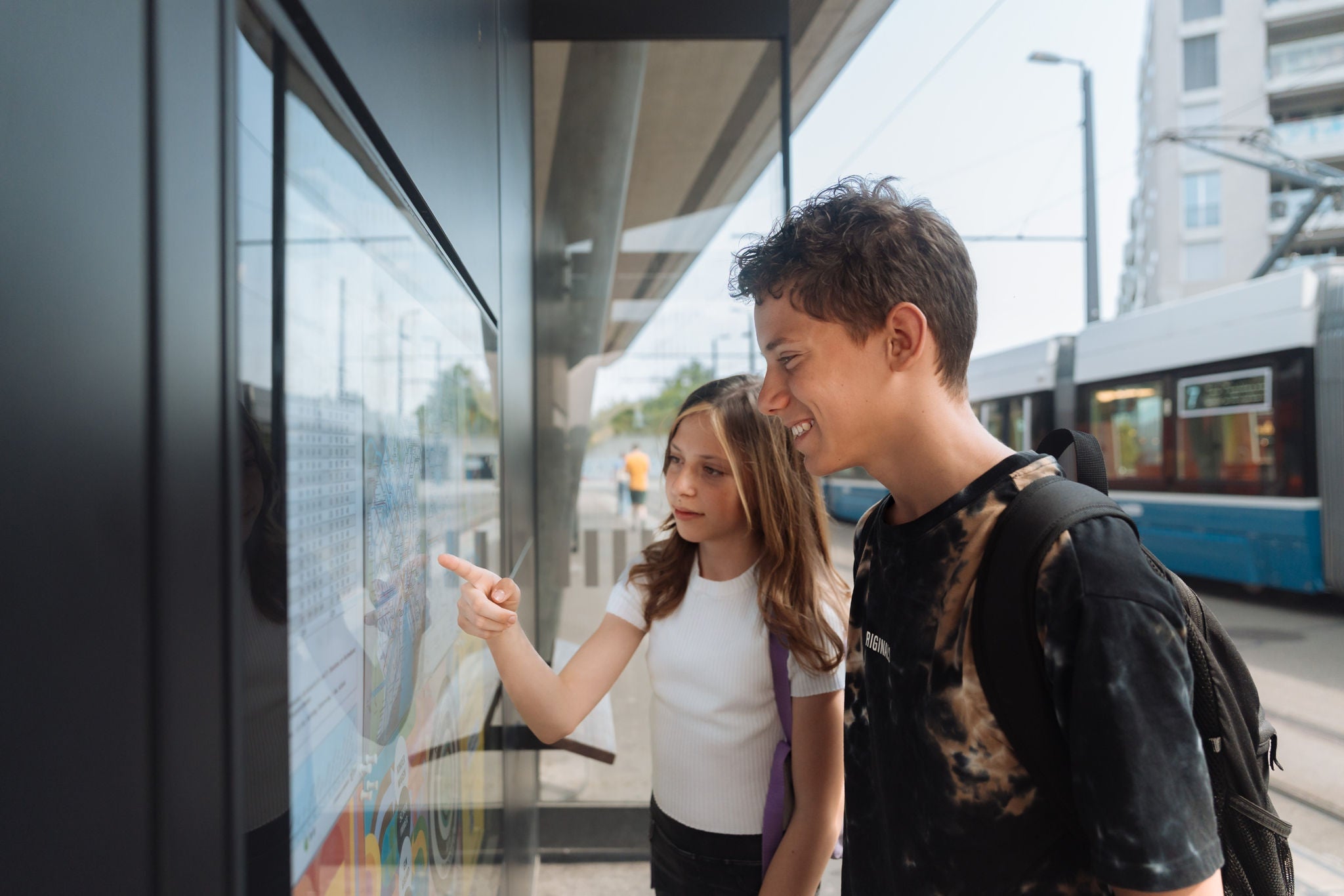 Eine Schülerin und ein Schüler studieren den Fahrplan an der Tram-Haltestelle.