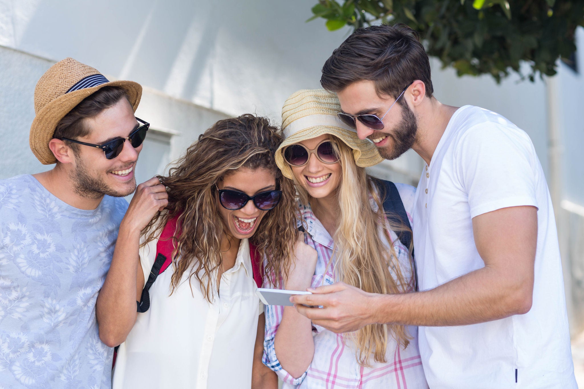 Vier Freunde mit Sonnenbrillen schauen in ein Smartphone.