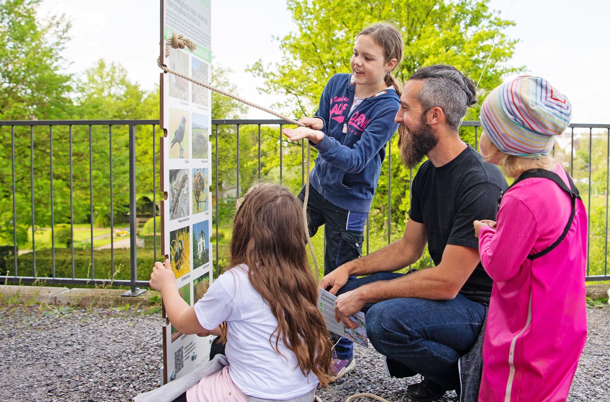 Vater mit drei Kindern vor einer Informationstafel. 