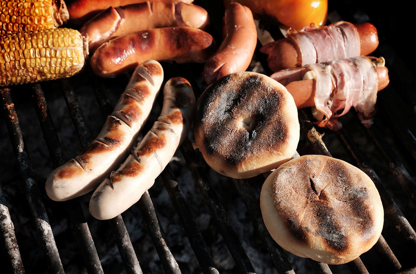 Würste, Mais und Brötchen auf dem Grillrost