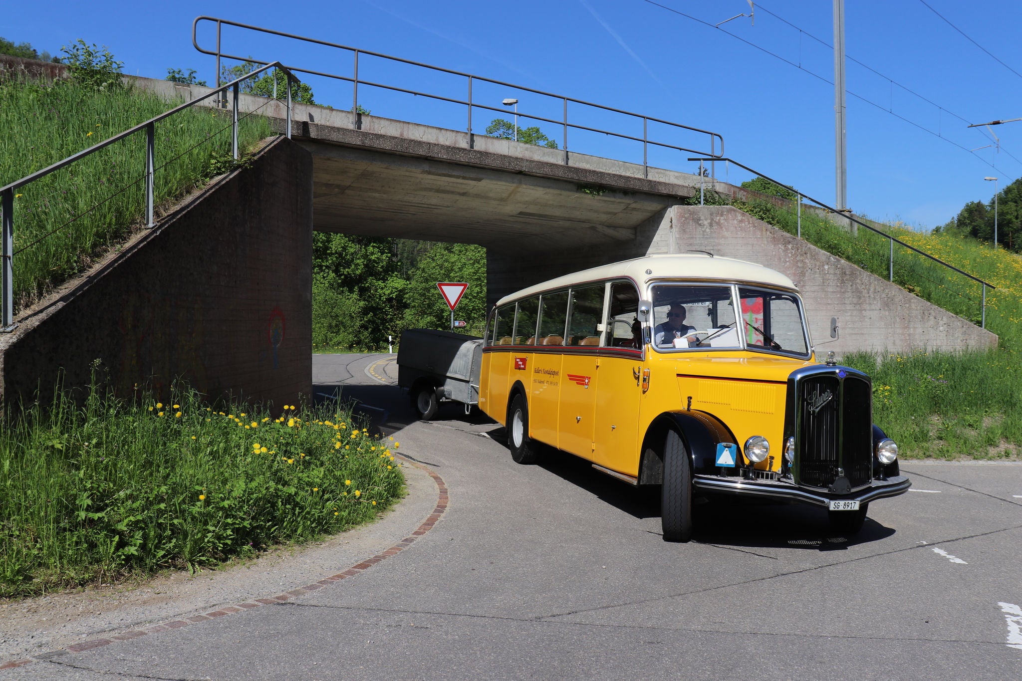 Ein Oldtimer Postauto fährt unter einer Zugunterführung durch. 