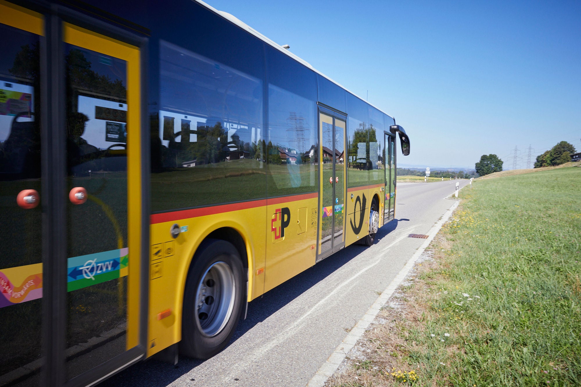 Postauto fährt im Sommer auf Landstrasse.
