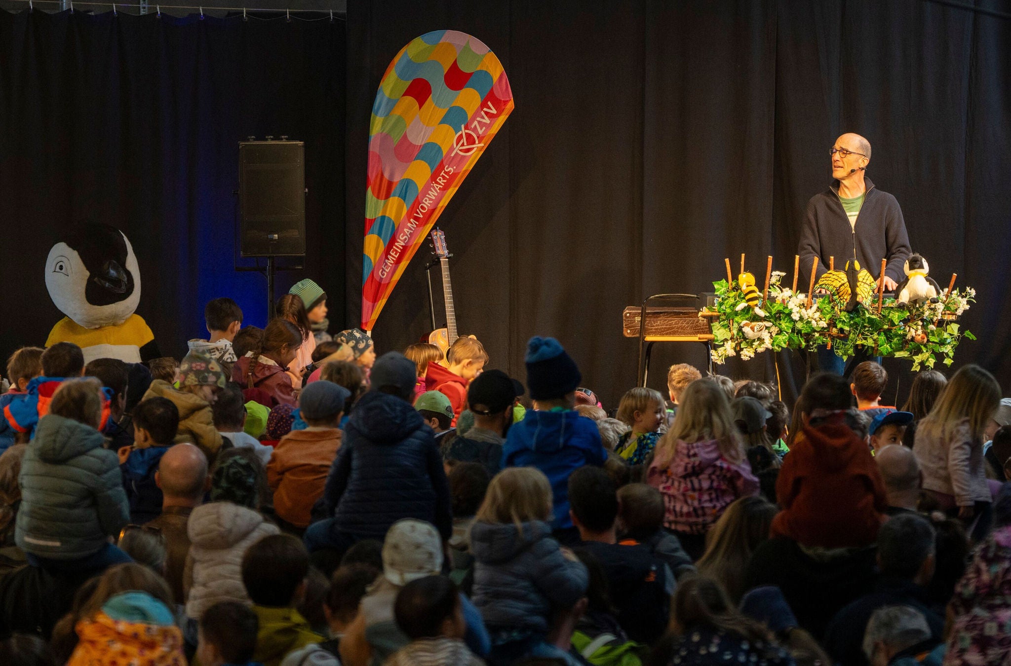 Andrew Bond singt auf der Bühne vor vielen Kindern. 