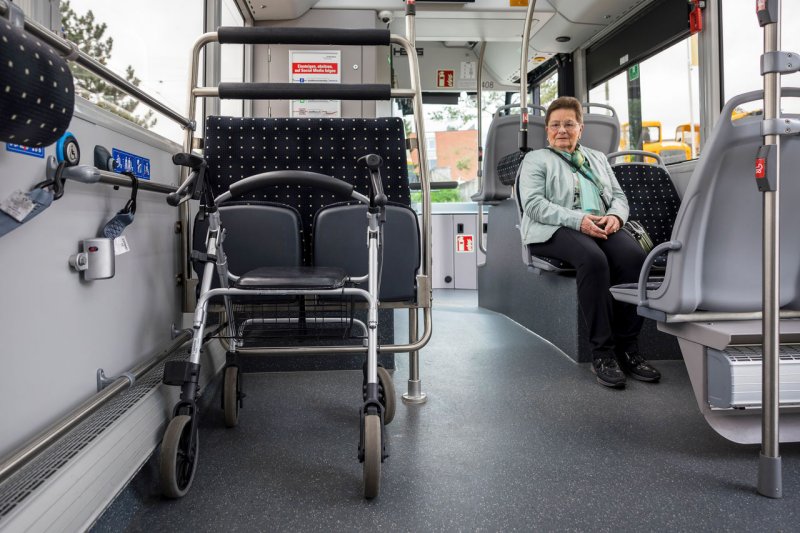 Eine Seniorin sitzt im Bus mit Blick auf ihren richtig platzierten Rollator. 