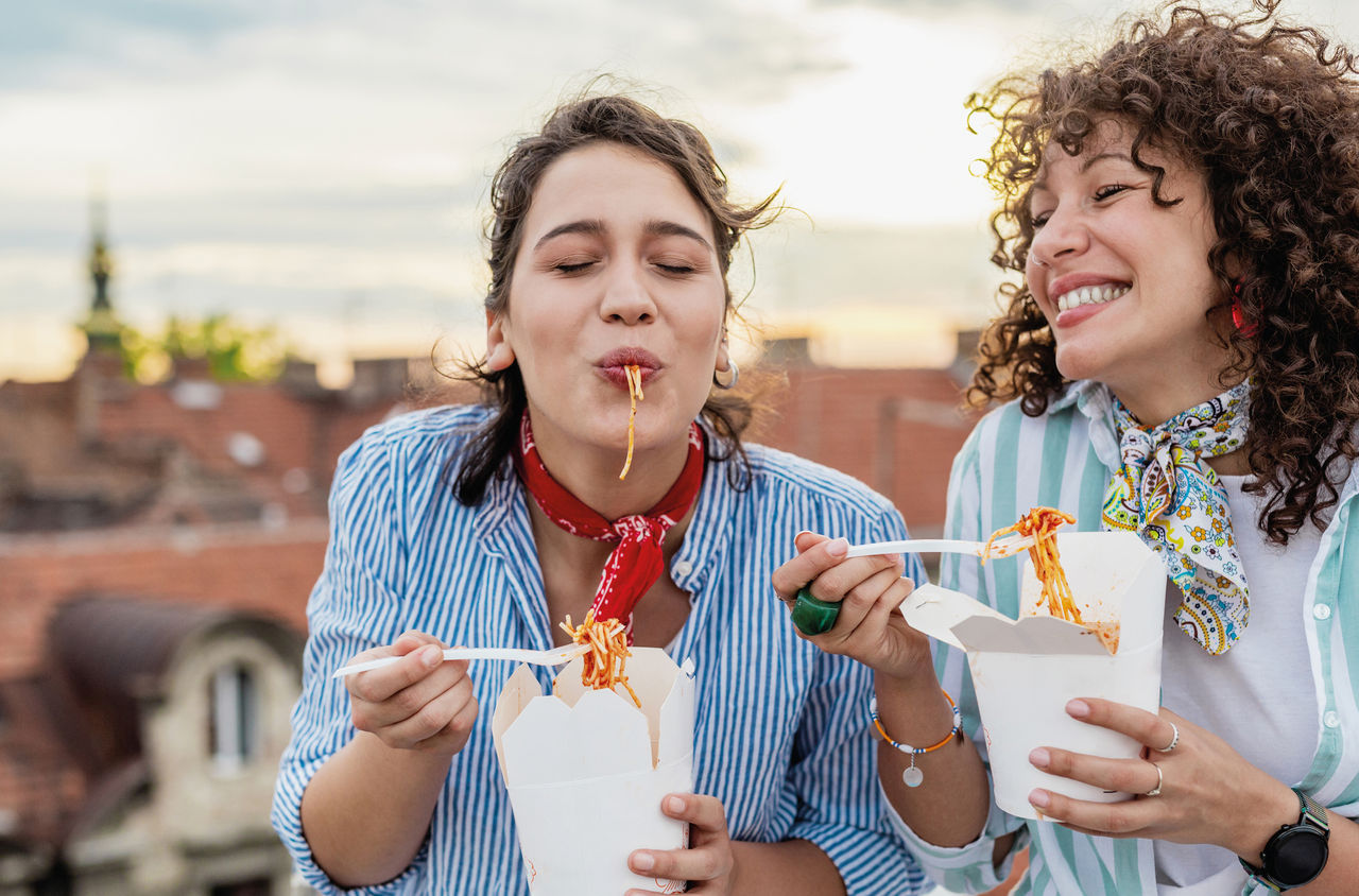 Zwei Freundinnen essen Pasta aus einem Takeaway-Behälter. 