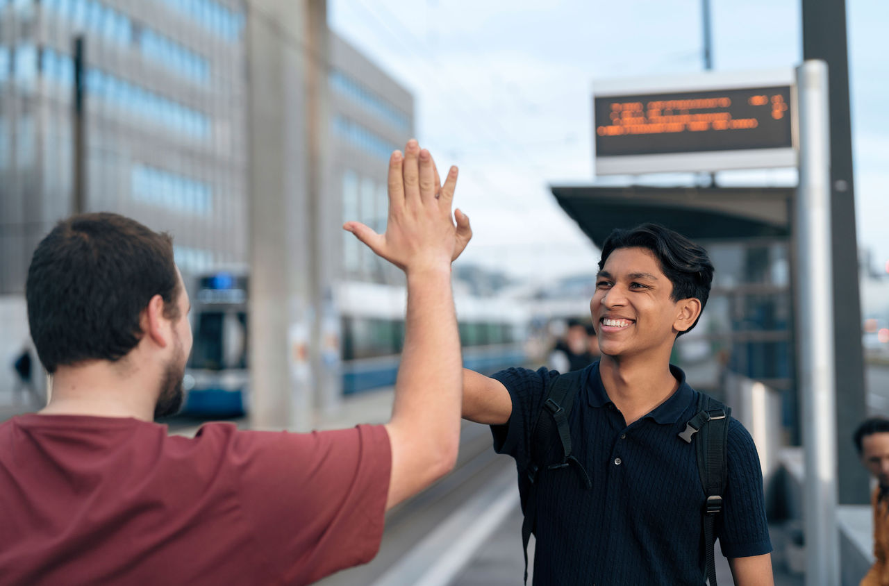 Zwei jugendliche klatschen ab an der Tramhaltestelle