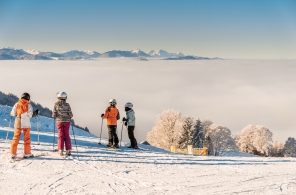 Kinder stehen auf der Piste des Skigebietes Atzmännig und blicken übers Nebelmeer.