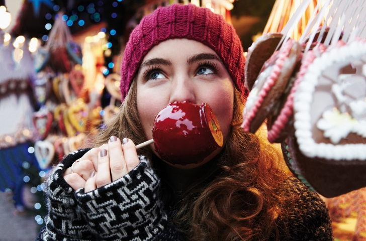 Eine Frau am Weihnachtsmarkt beisst in einen karamellisierten Apfel. 