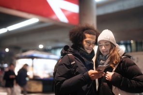 Paar steht am Bahnhof und schaut aufs Smartphone.