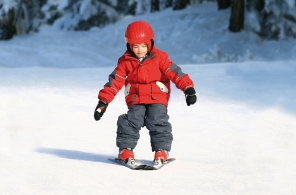 Ein Kind lernt auf einer flachen Piste Skifahren. 