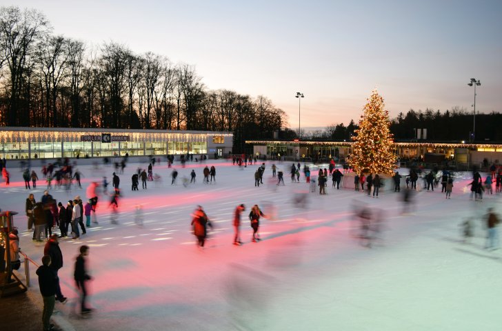 Personen am Eislaufen auf der Dolder Kunsteisbahn in Zürich, auf der ein geschmückter Christbaum steht.