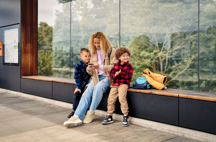 Eine Mutter mit zwei Kindern wartet an der Haltestelle und informiert sich über allfällige Störungen in der ZVV-App.