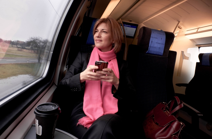 Eine Frau sitzt in der S-Bahn mit dem Mobiltelefon in der Hand